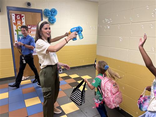 counselor creating bubbles from hand-held  dispenser as students walk by